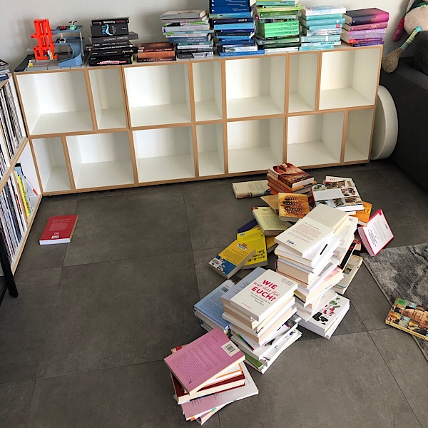Leeres weisses Bücherregal mit bunten Bücherstapeln 