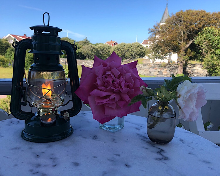 Lampe mit Feier, pinke Pfingstrose und im Hintergrund Kirche und Garten 