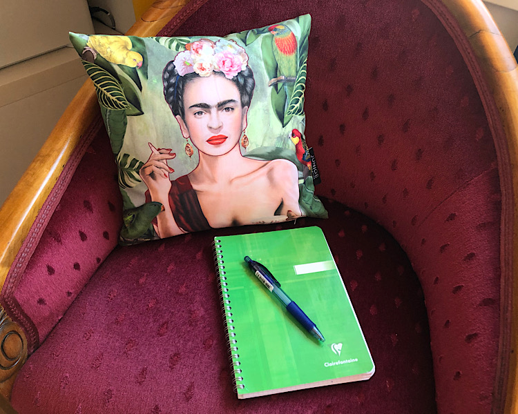 Roter Sessel mit grünem Kollegheft, Stift und Kissen Frida Kahlo